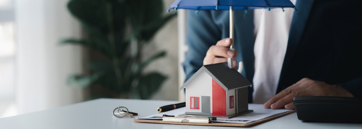 Man achter een bureau houdt een paraplu boven een woning waaronder een formulier ligt