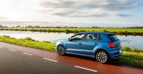Een blauwe auto staat geparkeerd langs de kant van de weg op een bewolkte dag in Nederland.
