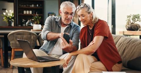 Een ouder stel kijkt op een telefoon en laptop